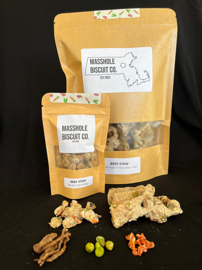 Masshole Biscuit Co all natural dog treat combo bag. In this picture you can see the training treat bag next to Massachusetts state shaped treat bag. Both treats are featured along side USDA beef, peas, and carrots, which serve as the chunky style add ins to the dog treat dough. The Masshole Dog treat package is beige featuring the Masshole Biscuit Co logo and the dog treat flavor, beef stew. Their is a clear window where you can see the Massachusetts state shaped treats.
