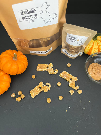 Homemade all natural dog treats made with whole ingredients like pumpkin and peanut butter. Treats are shaped like Massachusetts with holes in the middle. The holes are repurposed to make Masshole dog treats. This picture shows the packaging and the treats. Dog cookie, dog treat, dog snack. Masshole Biscuit Co.